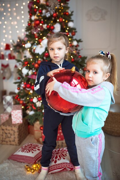 Ein kleines mädchen hält eine große rote glaskugel für den weihnachtsbaum