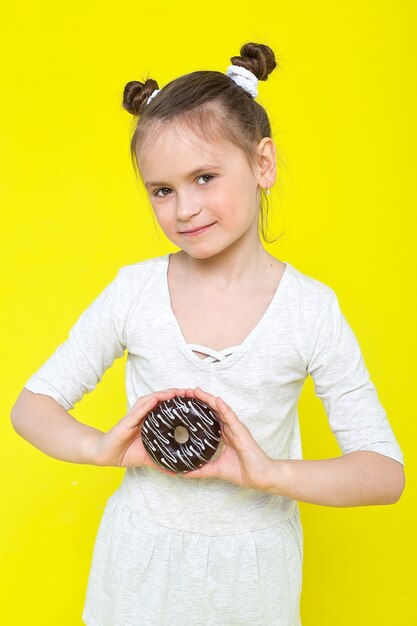 Foto ein kleines mädchen hält einen donut in heller glasur.