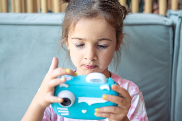 Ein kleines Mädchen hält in ihren Händen eine blaue Spielzeug-Digitalkamera für Kinder zum sofortigen Fotodruck.