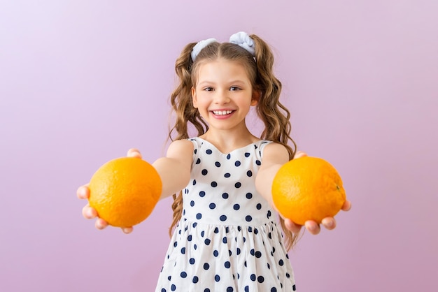 Ein kleines Mädchen hält Orangen und lächelt breit Ein schönes Kind in einem Polka-Dot-Kleid auf einem rosa isolierten Hintergrund Citrus-Vitamine für Kinder