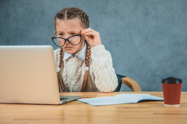 Ein kleines Mädchen hält seine schwarze Brille mit der linken Hand und versteht das Thema auf dem Laptop nicht