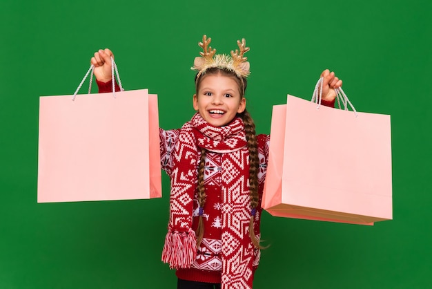 Ein kleines Mädchen hält Taschen mit Geschenken für Weihnachten Weihnachtsrabatte in Geschäften für den Urlaub Kinder in einem Neujahrspullover mit Taschen aus dem Laden