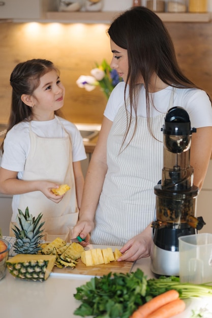 Ein kleines Mädchen hilft ihrer Mutter in der Küche. Frauen schneiden Ananas für frischen hausgemachten Saft.