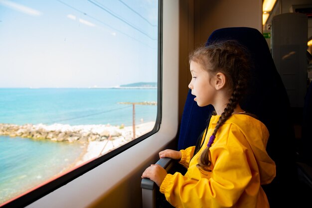 Ein kleines Mädchen im Alter von 6-7 Jahren schaut aus dem Fenster eines Zuges auf das Meer. Familienurlaub.