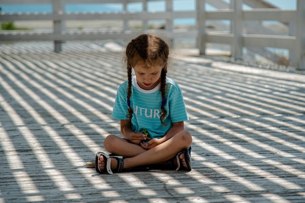 Ein kleines Mädchen im Schatten eines Pavillons spielt mit Steinen Sie spielt mit Licht und Schatten Kindheit