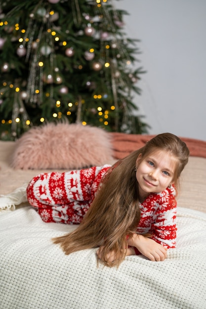 Ein kleines Mädchen im Schlafanzug fand am frühen Morgen ein Geschenk des Weihnachtsmanns unter dem Baum. Weihnachtszaubermärchen. Glückliche Kindheit.