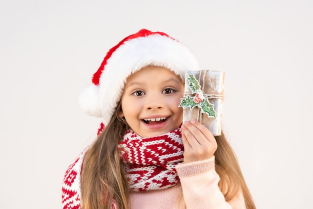 Ein kleines Mädchen im Weihnachtsoutfit und einem rot-weißen Schal zeigt ihr Geschenk.