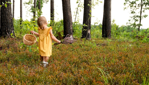 Ein kleines Mädchen in einem gelben Kleid geht mit einem Strauß Heidekraut im Wald spazieren