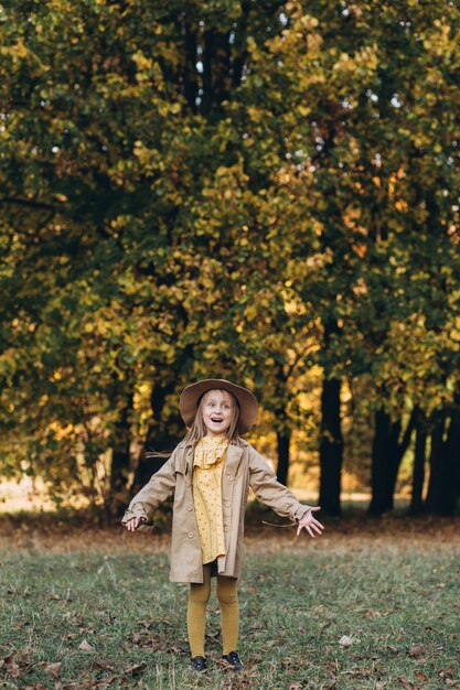 Ein kleines Mädchen in einem gelben Kleid und einem beigen Mantel gehen im Herbstpark spazieren