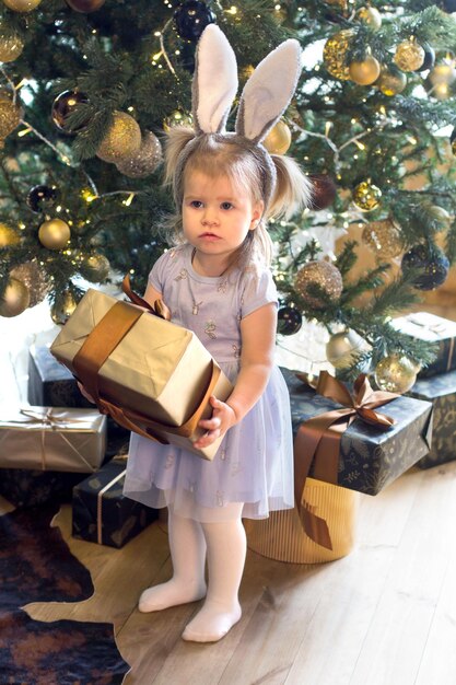 Ein kleines Mädchen in einem Häschenkostüm nahe einem Weihnachtsbaum mit Geschenken