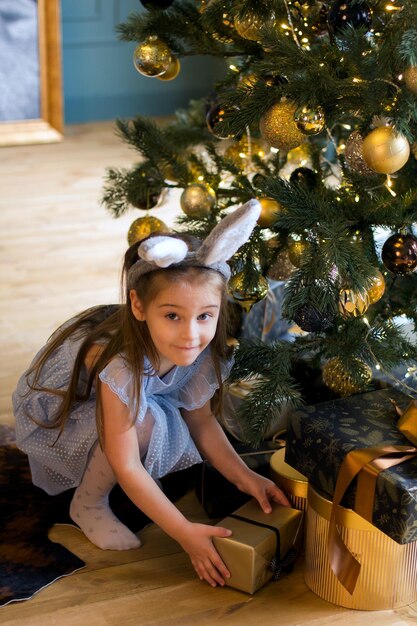 Foto ein kleines mädchen in einem häschenkostüm nahe einem weihnachtsbaum mit geschenken