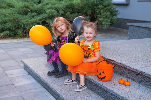 Ein kleines Mädchen in einem Halloween-Kostüm sitzt mit Bällen in den Händen im Freien