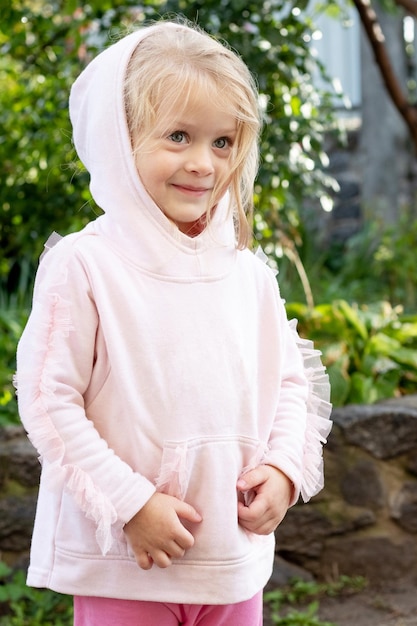 Ein kleines Mädchen in einem Kapuzenpullover mit einem schüchternen Lächeln in der Natur