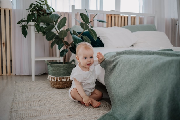 Ein kleines Mädchen in einem Musselin-Overall sitzt auf einem Teppich im Schlafzimmer auf dem Boden