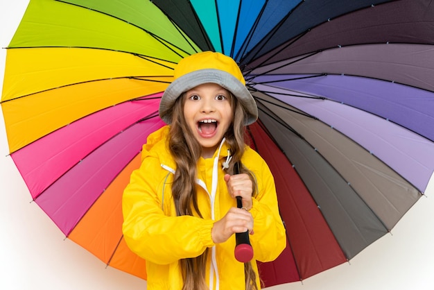 Ein kleines Mädchen in einem Regenmantel hält einen bunten Regenschirm auf einem weißen, isolierten Hintergrund Regenwetter