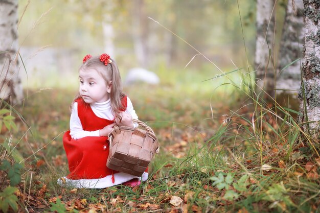 Ein kleines Mädchen in einem roten Hut und Kleidern geht im Park spazieren. Cosplay für den Märchenhelden "Rotkäppchen"
