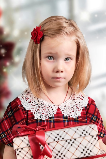 Ein kleines Mädchen in einem roten Kleid sitzt am Tisch und schreibt einen Brief an die Weihnachtsmannskarte