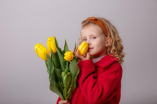 Ein kleines Mädchen in einem roten Mantel hält einen Blumenstrauß aus Frühlingstulpen auf weißem Hintergrund