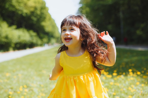 Ein kleines Mädchen in einem sommergelben Kleid fängt Seifenblasen auf dem Gras im Parkkranz aus Löwenzahn