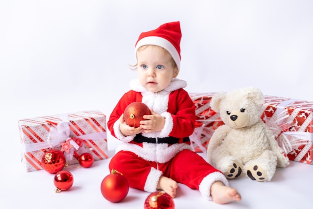 Ein kleines Mädchen in einem Weihnachtsmannkostüm sitzt mit Neujahrsgeschenken in Kisten auf weißem Hintergrund