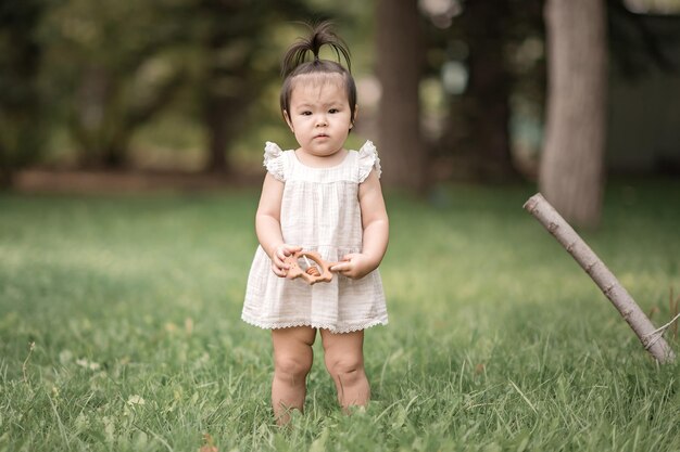 Ein kleines Mädchen in einem weißen Kleid mit asiatischem Aussehen steht im Sommer im Wald