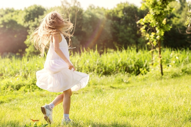 Ein kleines Mädchen in einem weißen Kleid tanzt auf dem Gras