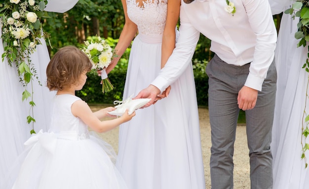 Ein kleines Mädchen in einem weißen Kleid trägt Eheringe auf hellem Kissen