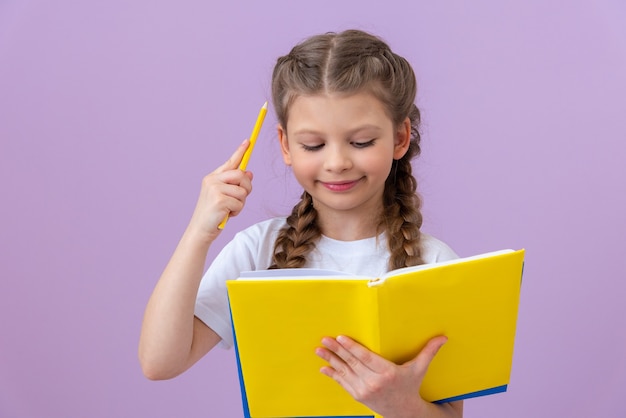 Ein kleines Mädchen in einem weißen T-Shirt liest ein Buch auf einem isolierten Hintergrund.