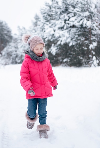 Ein kleines Mädchen in einer hellen Jacke spielt im verschneiten Winterwald.