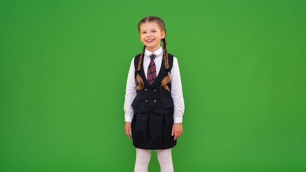 Ein kleines Mädchen in einer Schuluniform auf einem grünen Hintergrund kopieren Raum