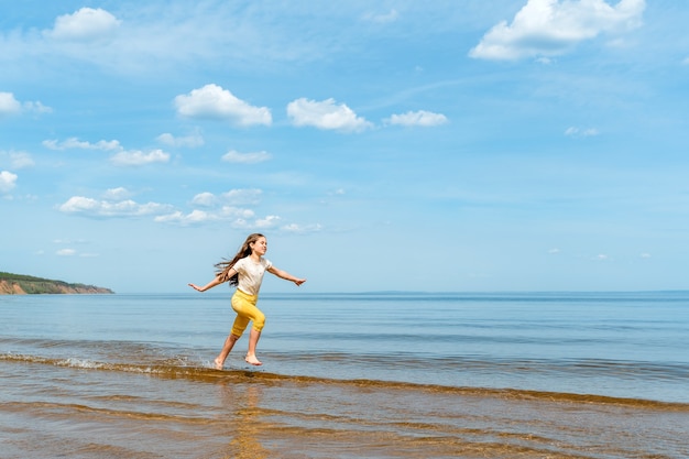 Ein kleines Mädchen in knallgelber Hose läuft im Wasser und tobt am Strand