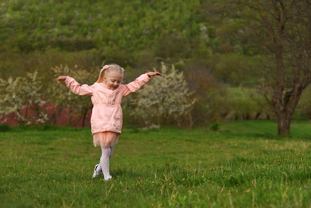 Ein kleines Mädchen in rosa Kleidung läuft auf einer grünen Wiese, ein Kind geht durch eine Lichtung im Spring Park.