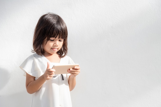 Ein kleines Mädchen konzentriert sich auf den Telefonblick auf das Smartphone-Technologiekonzept für Kinder