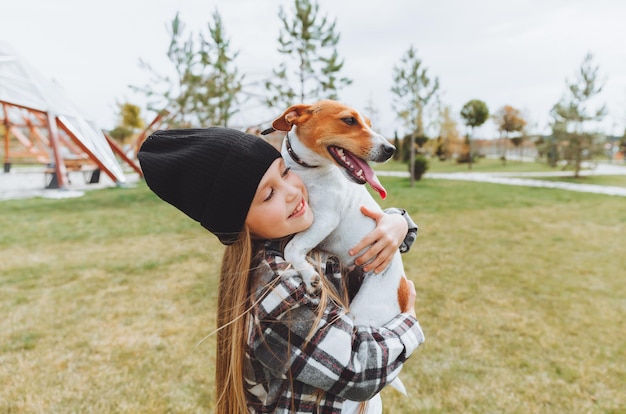 Ein kleines Mädchen küsst und umarmt ihren Jack Russell Terrier Hund im Park Liebe zwischen dem Besitzer und dem Hund ein Kind hält einen Hund in seinen Armen