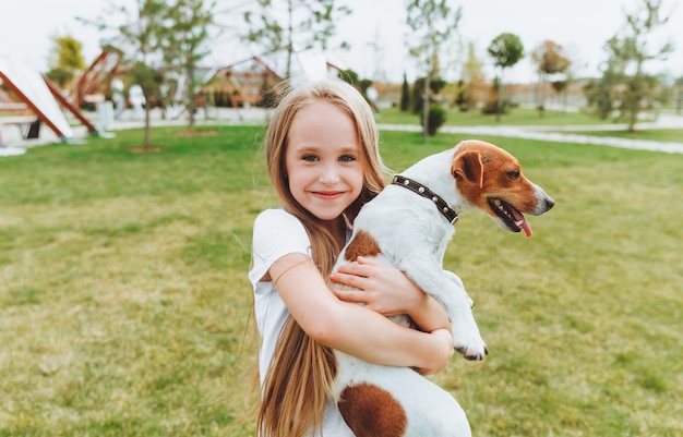 Ein kleines Mädchen küsst und umarmt ihren Jack Russell Terrier Hund im Park Liebe zwischen dem Besitzer und dem Hund ein Kind hält einen Hund in seinen Armen