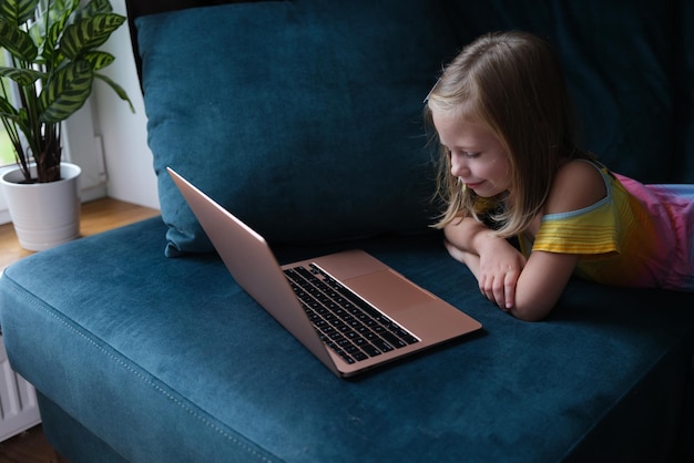 Ein kleines Mädchen liegt mit einem Laptop auf der Couch