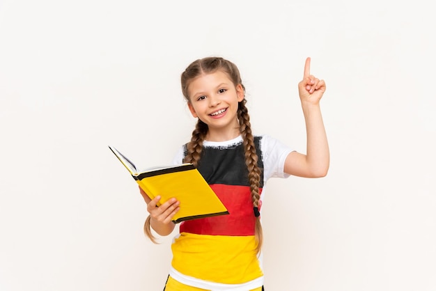 Ein kleines Mädchen liest ein Buch auf Deutsch und zeigt auf Ihre Werbung Kurse für den Deutschunterricht für Kinder Ein Kind in einer Jacke mit einer deutschen Flagge auf einem weißen, isolierten Hintergrund