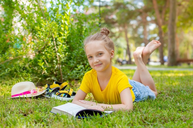 Ein kleines Mädchen liest im Sommer ein Buch auf der Wiese im Park