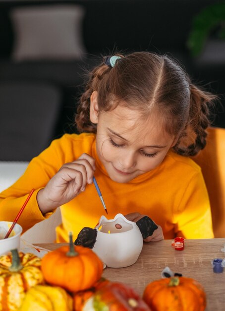 Ein kleines Mädchen malt einen aus Ton handgefertigten Kürbis Halloween-Party-Handwerk für Kinder