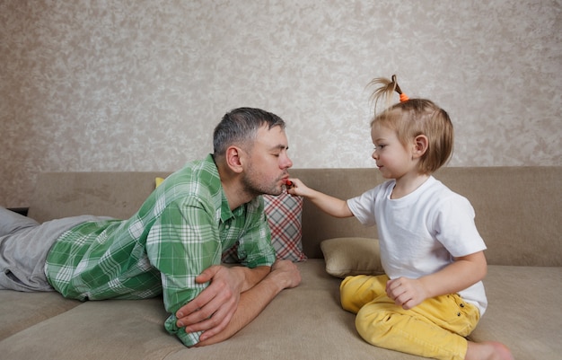 Ein kleines Mädchen malt ihrem Vater ihre Lippen mit hellem Lippenstift