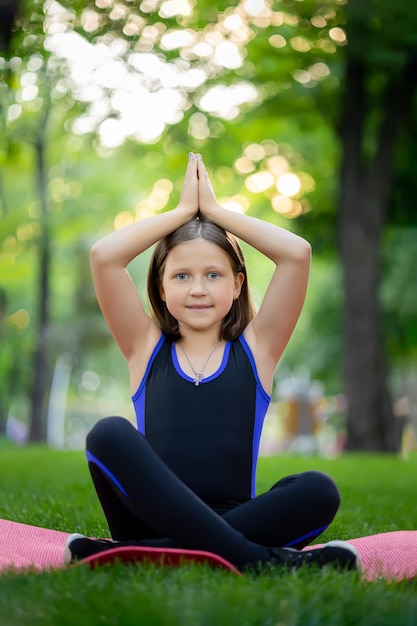 Ein kleines Mädchen meditiert im Park in der Lotusposition, das Mädchen macht Yoga, hob die Hände und faltete die Handflächen