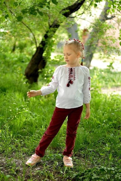 Ein kleines Mädchen mit Blumen in einem ukrainischen bestickten Hemd im Park