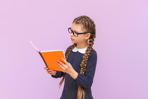 Ein kleines Mädchen mit Brille hält Lehrbücher in den Händen und lächelt breit auf einem rosa isolierten Hintergrund Bildungskurse für Schulkinder