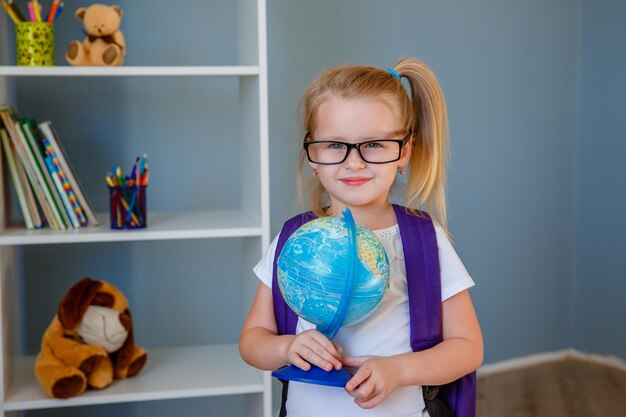 Ein kleines Mädchen mit Brille und Rucksack hält in der Schule einen Globus