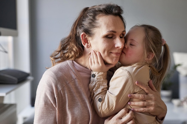 Ein kleines Mädchen mit Down-Syndrom küsst seine Mutter