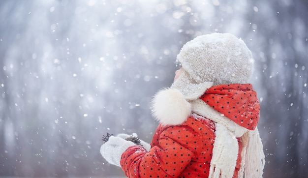 Ein kleines Mädchen mit einem flauschigen Hut geht an einem verschneiten Wintertag spazieren
