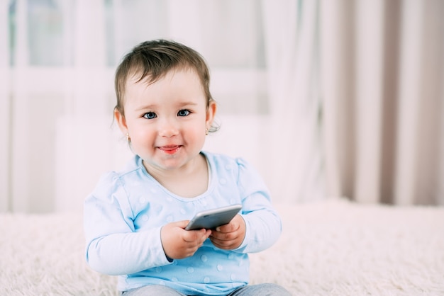 Ein kleines Mädchen mit einem Smartphone in den Händen sitzt und drückt