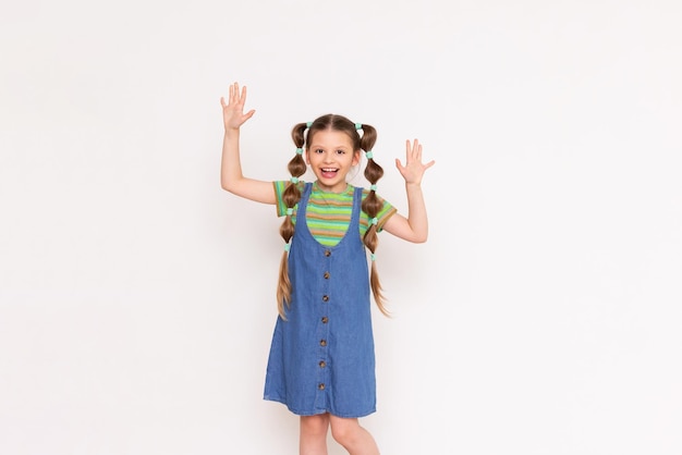 Ein kleines Mädchen mit einer lustigen Frisur zeigt mit ihren Handflächen auf Ihre Werbung auf einem weißen, isolierten Hintergrund Ein Kind in einem sommerlichen Denim-Sommerkleid