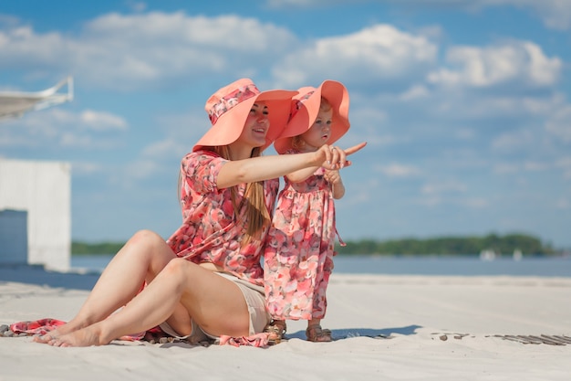 Ein kleines Mädchen mit ihrer Mutter in passenden schönen Sommerkleidern spielt im Sand am Strand. Stilvoller Familienlook.