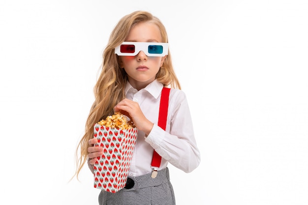 Ein kleines Mädchen mit Make-up und langen blonden Haaren mit Popcorn und 3D-Brille